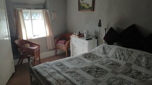 A bedroom with a bed, a chair, a dresser, and a window with curtains. - Southern Cross Guest House (Sidmouth)
