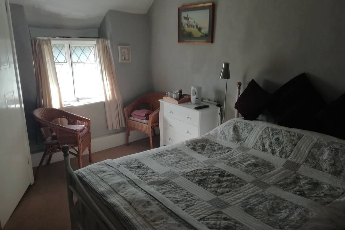 A bedroom with a bed, a chair, a dresser, and a window with curtains.