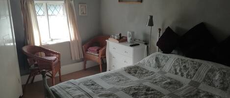 A bedroom with a bed, a chair, a dresser, and a window with curtains.