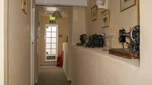 A hallway with a fire exit sign, a fire extinguisher, and vintage sewing machines on a counter. - Southern Cross Guest House (Sidmouth)