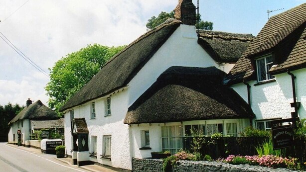 A traditional white building with a thatched roof, a stone wall, and a sign indicating it is a pub. - Southern Cross Guest House (Sidmouth)