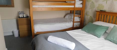 Habitación con literas, cabecera de madera, mesita de noche pequeña de madera con botellas, colcha de cama texturizada de color gris y almohada verde.