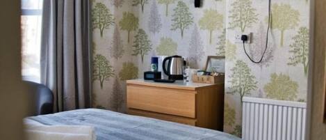 A hotel room with a bed, a wooden dresser, a flat-screen TV mounted on the wall, and a window with curtains.