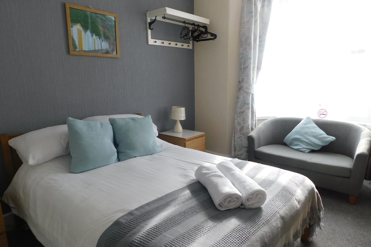 Een hotelkamer met een bed, een stoel, een nachtkastje, een lamp, een schilderij en een raam met gordijnen.