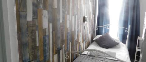 A bedroom with a metal bed frame, a patterned wall, and a window with curtains.