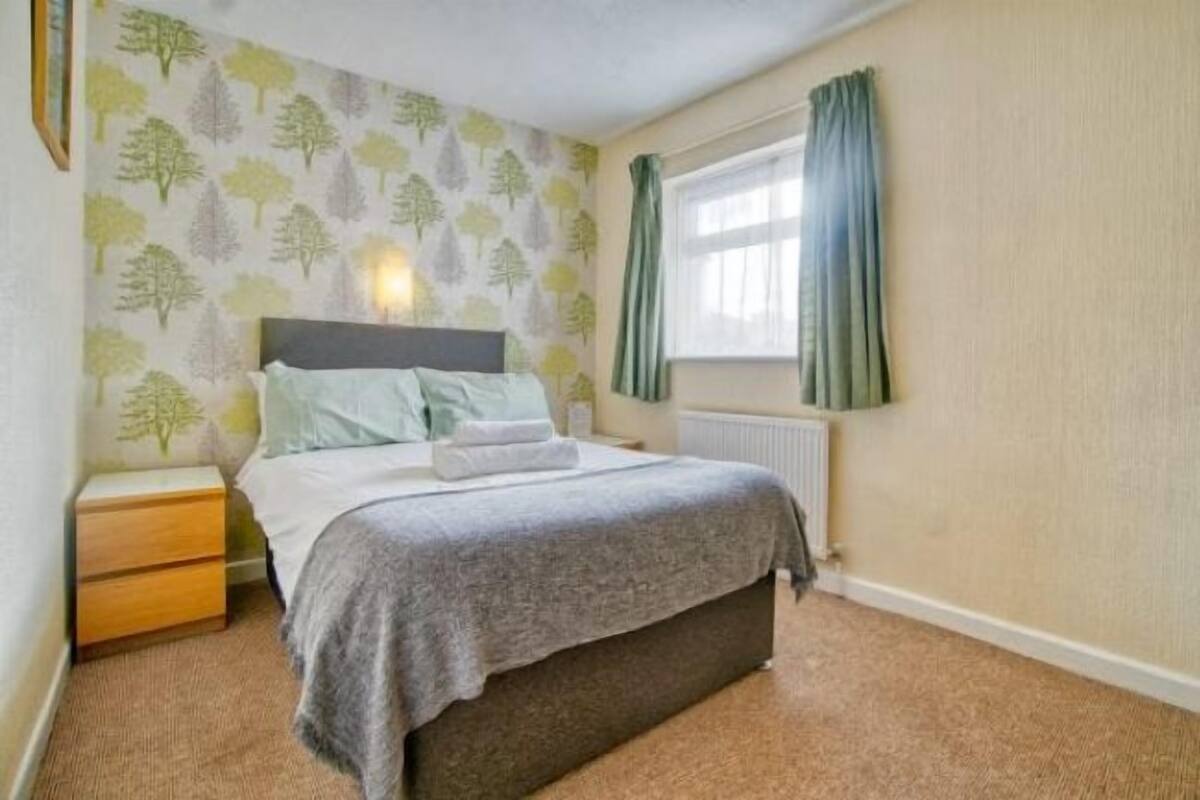 Een slaapkamer met een bed, nachtkastje en een raam met gordijnen.