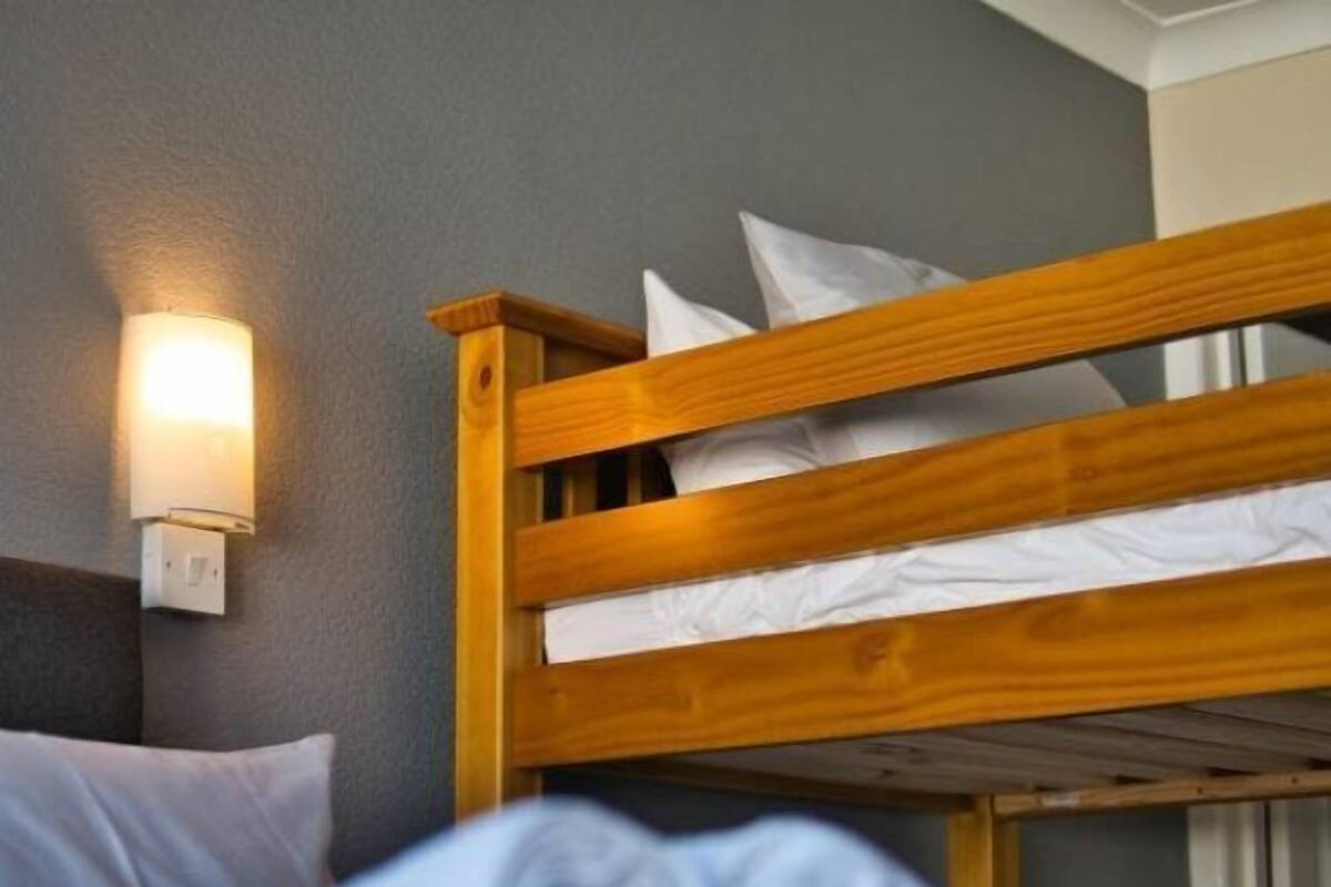 Een stapelbed met witte beddengoed en een wandlamp.