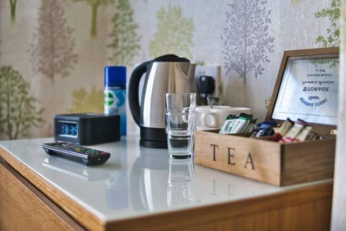 Een hotel receptiebalie met een koffiezetapparaat, een glas water, een klok, een theedoos en een menukaart in een lijst.
