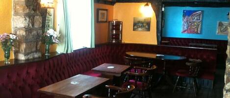 Un restaurante acogedor con un banco tapizado en terciopelo rojo, mesas y sillas de madera.
