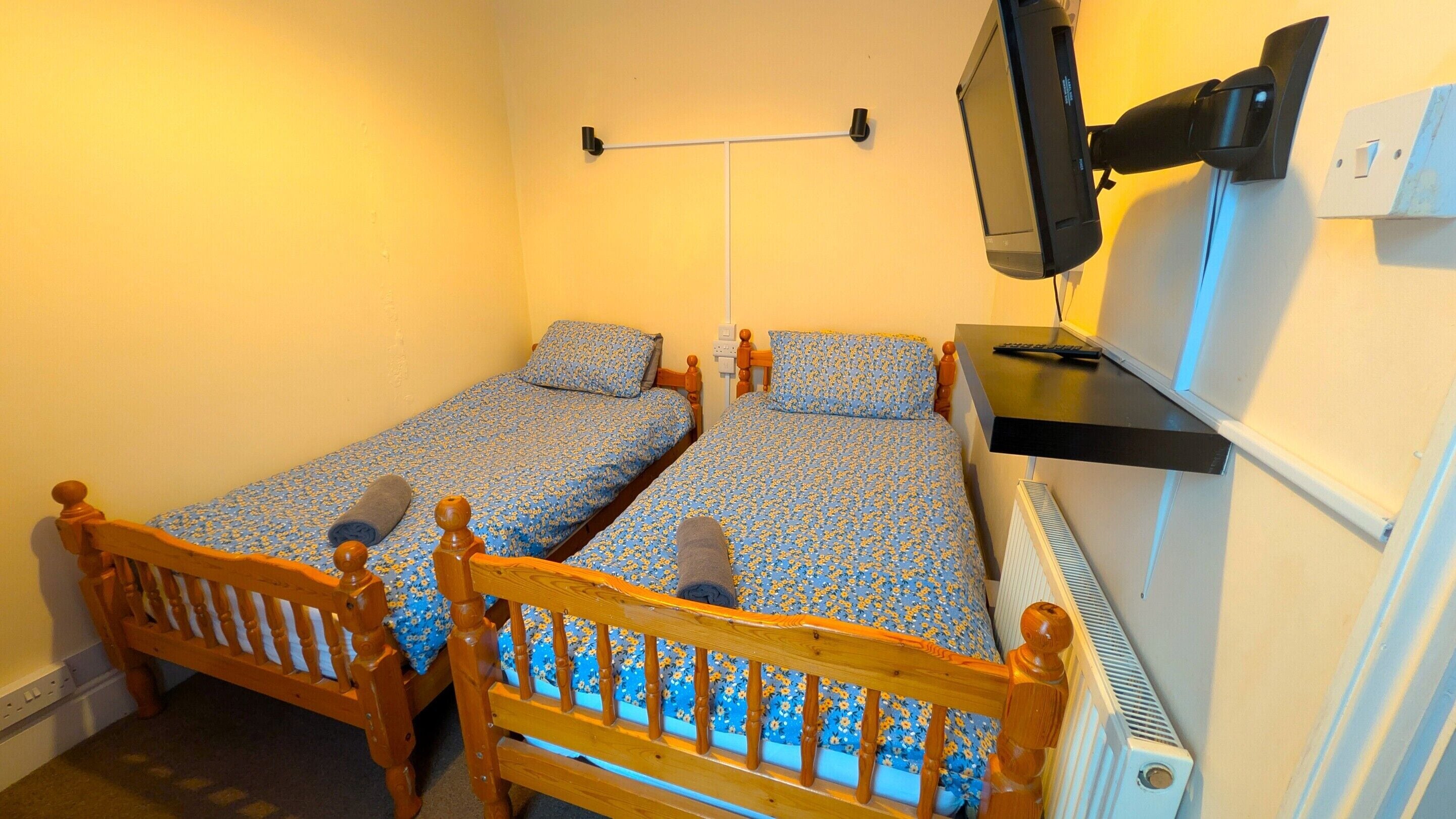 A small room with two wooden beds, a TV mounted on the wall, and a radiator.
