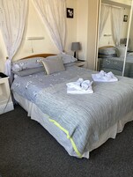 Una cama bien hecha con ropa de cama floral, una lámpara de noche y un espejo que refleja la habitación.