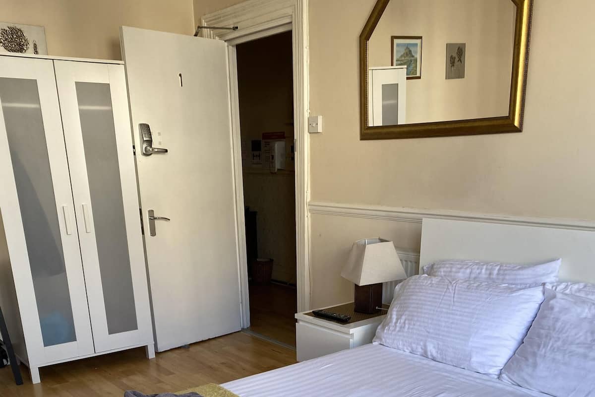 Una habitación de hotel con cama, armario, mesita de noche y un espejo en la pared.