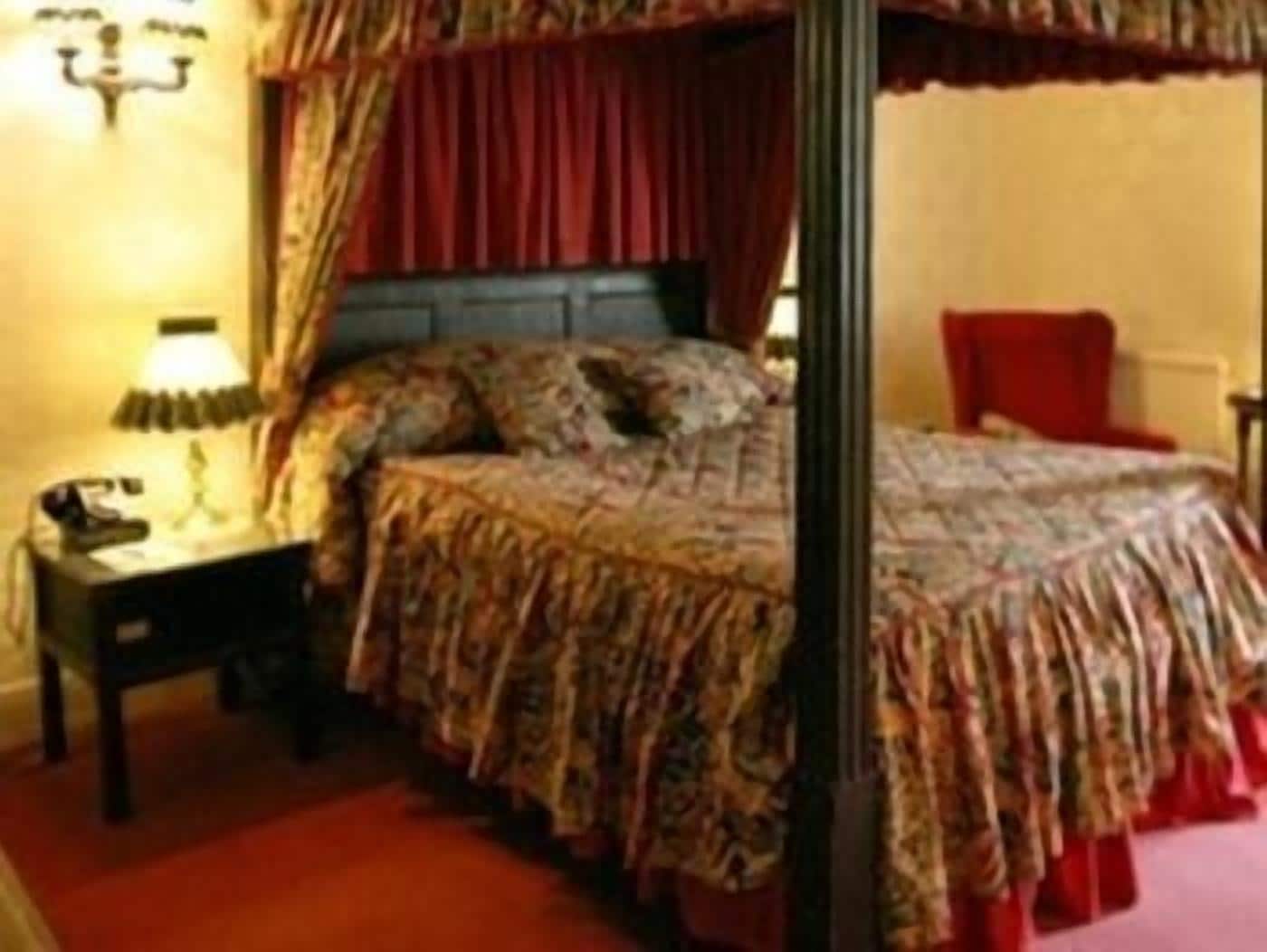 Une chambre à coucher avec un lit à baldaquin, une table de chevet avec une lampe et un fauteuil rouge.
