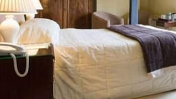 A neatly made bed with a white comforter and a brown throw blanket. There is a bedside table with a lamp and a telephone.