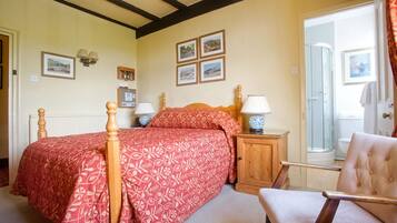 Quarto com uma cama grande, mesa de cabeceira de madeira, uma cadeira e porta para um banheiro.
