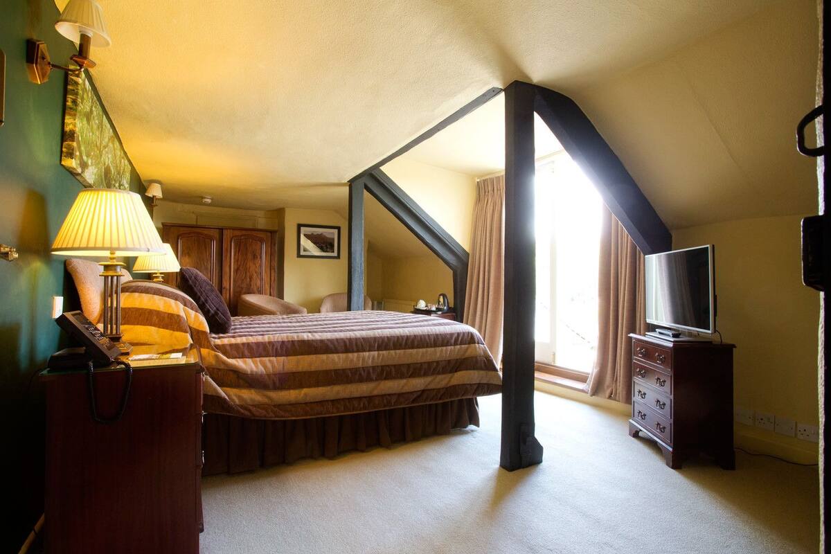 A bedroom with a bed, bedside lamps, a dresser, a television, and a window with curtains.