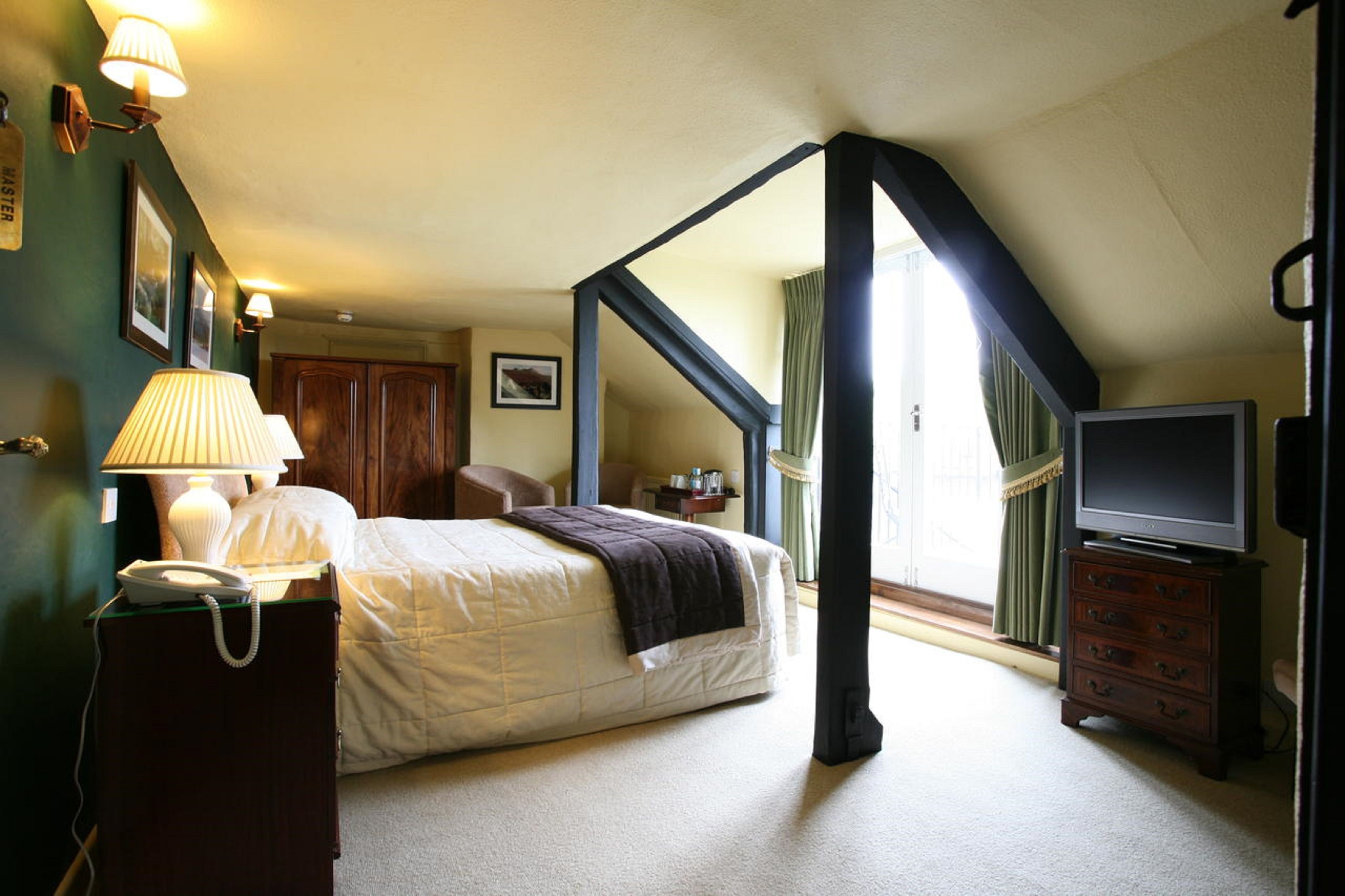 Et soveværelse med seng, kommode, fjernsyn og lampe.