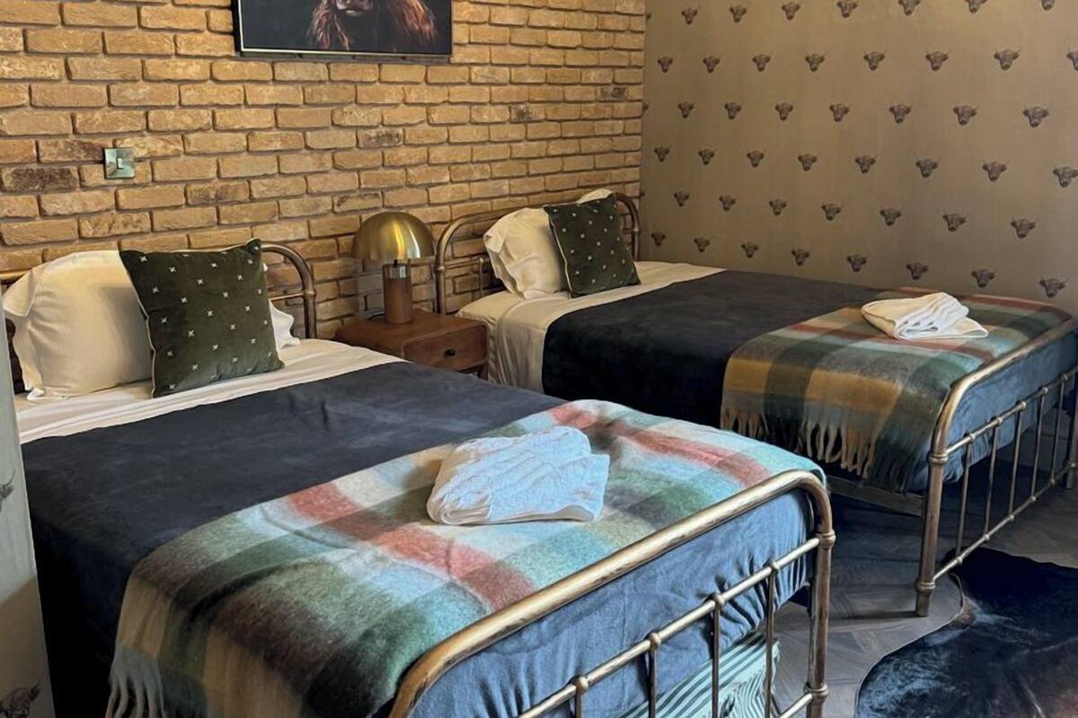 A hotel room with two beds, a brick wall, a framed picture, and patterned wallpaper.