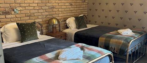 Una habitación de hotel con dos camas, una pared de ladrillo, un cuadro enmarcado y un papel tapiz estampado.
