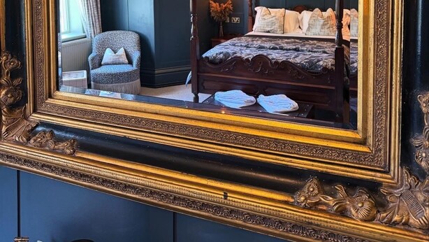 Une chambre à coucher avec un lit à baldaquin, une chaise et un grand miroir doté d’un cadre orné.