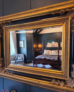 Quarto com cama de dossel, uma cadeira e um espelho grande com moldura decorada.