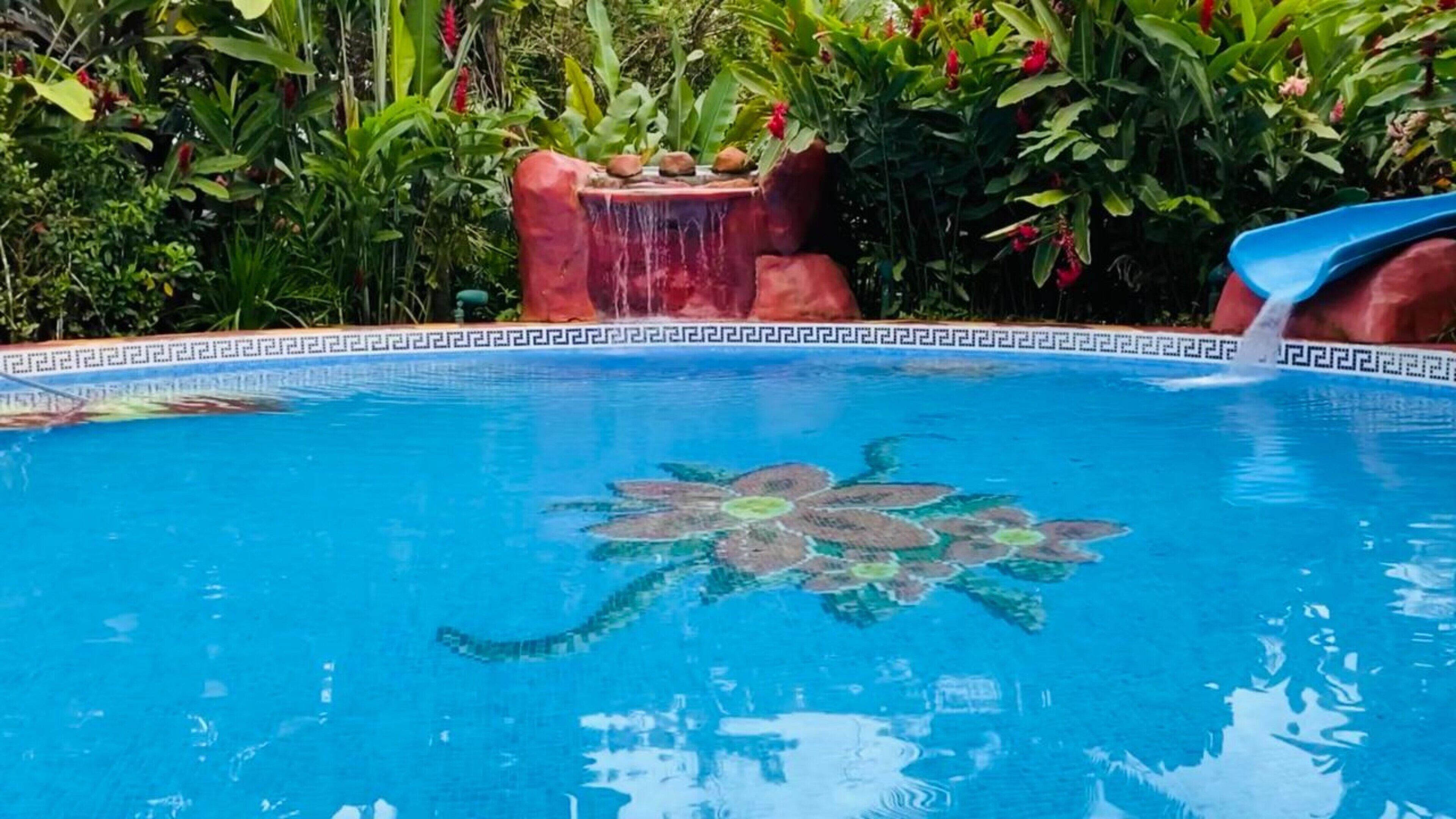 Una piscina con un diseño de azulejos decorativos, una fuente de agua y exuberante vegetación circundante.
