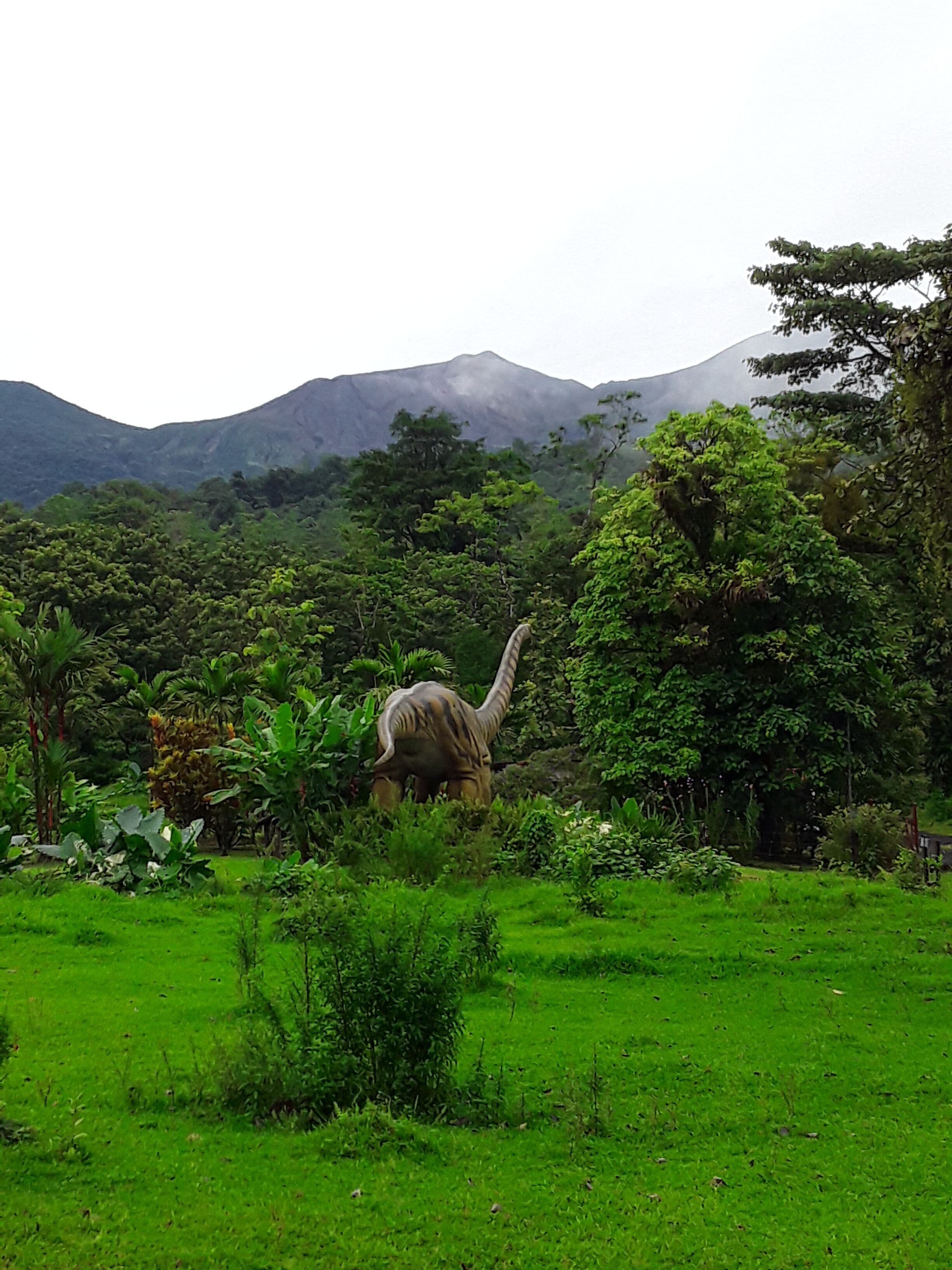 A dinosaur in a lush green landscape with mountains in the background.
