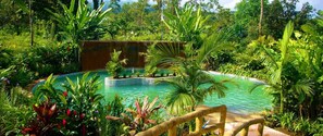 A lush garden with a circular pool surrounded by tropical plants and a wooden fence. - Blue River Resort & Hot Springs (Guayabo)