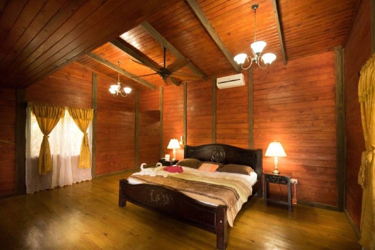 A wooden-paneled bedroom with a bed, two bedside tables with lamps, and a ceiling fan.