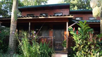 A wooden cabin with a porch, surrounded by lush greenery and trees.