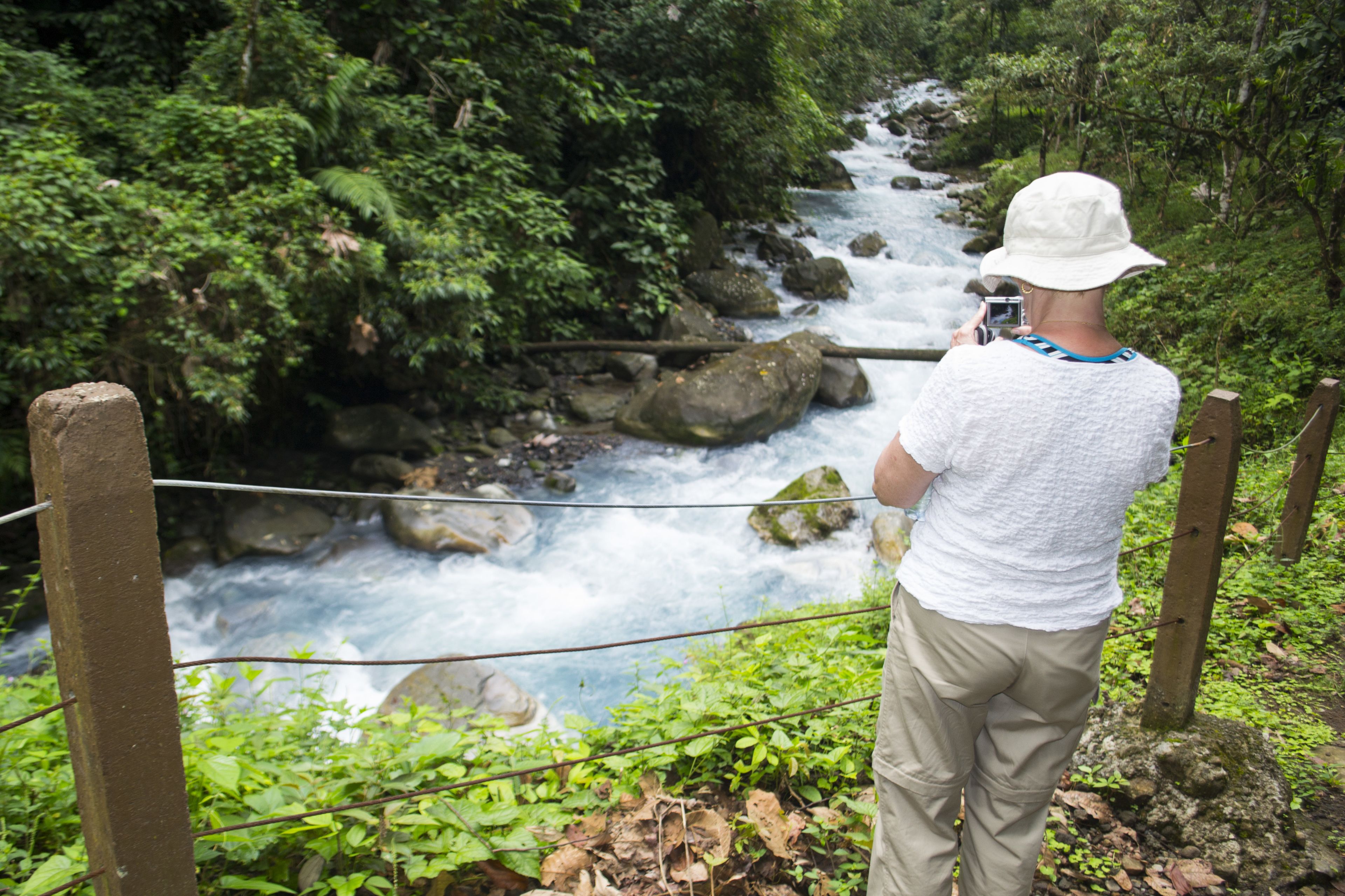 A person taking a photo of a river with a bridge in the background.
