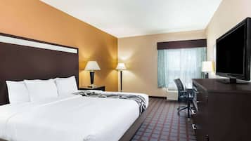 Una habitación de hotel con una cama grande, un escritorio con televisor, dos lámparas de noche y un ventanal con cortinas.