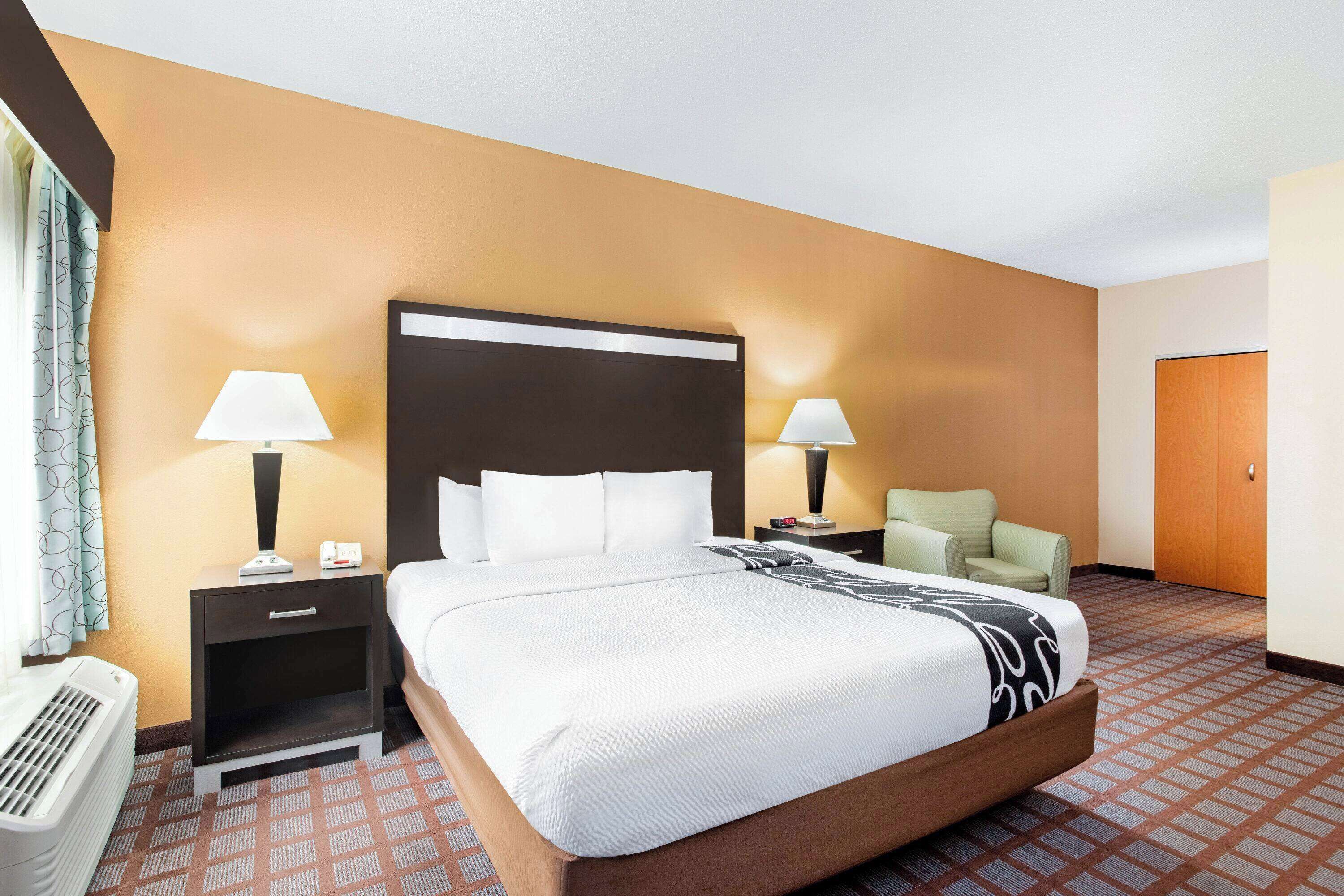 Ein Hotelzimmer mit einem großen Bett, zwei Nachttischen mit Lampen, einem Sessel, einem Heizkörper und einem Kleiderschrank.
