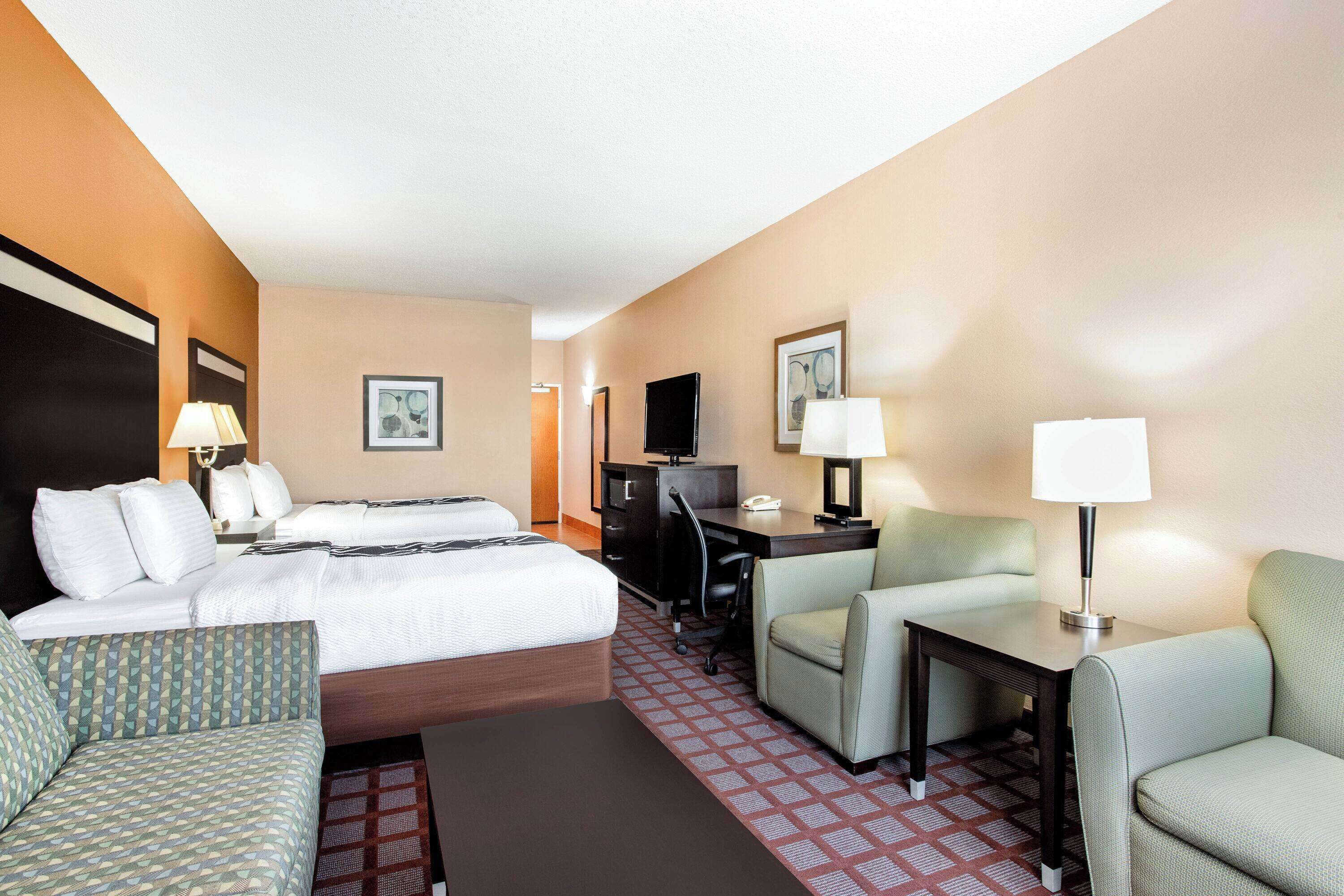 A hotel room with a bed, two armchairs, a desk, a TV, and a lamp.