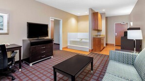 A hotel room with a television, a sofa, a desk, a cabinet, a bathtub, and a lamp.