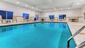 A swimming pool with chairs and tables, large windows, and a tiled ceiling.