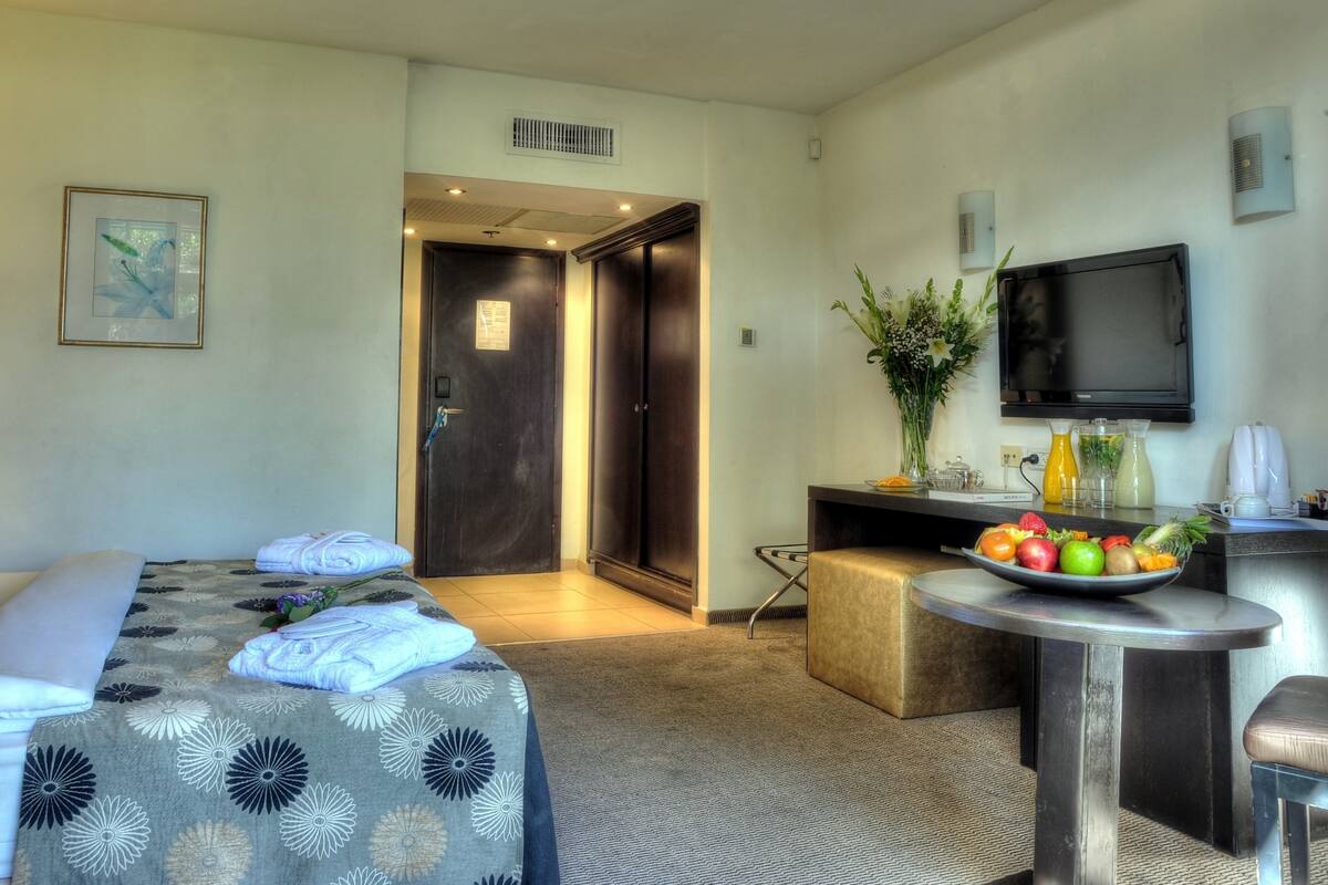 Une chambre d’hôtel avec un lit, un bureau sur lequel se trouve un panier de fruits, une télévision et une porte donnant sur une autre pièce.