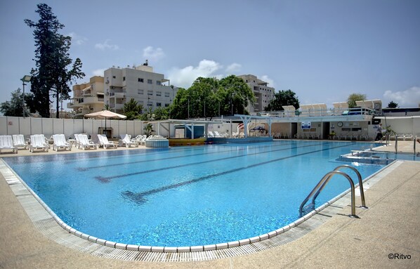 A swimming pool with lounge chairs, a changing room, and a building in the background.