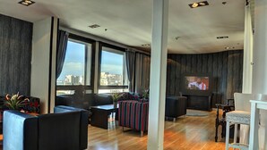 Un salon moderne doté d’un grand téléviseur, de sièges confortables et offrant une vue sur la ville.