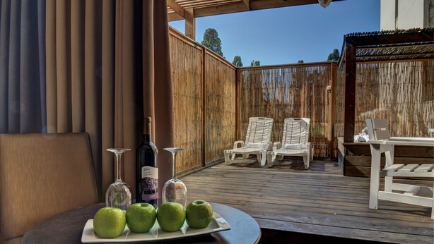 Une terrasse en bois avec un espace salon extérieur, comprenant deux chaises blanches et une table sur laquelle se trouve une assiette de pommes vertes et deux verres à vin.