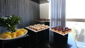 Une table de buffet garnie de divers desserts, une plante en pot et une vue sur l’extérieur par une fenêtre.