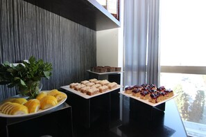 A buffet table with various desserts, a potted plant, and a view of the outdoors through a window. - Carlton Hotel Nahariya (Nahariya)