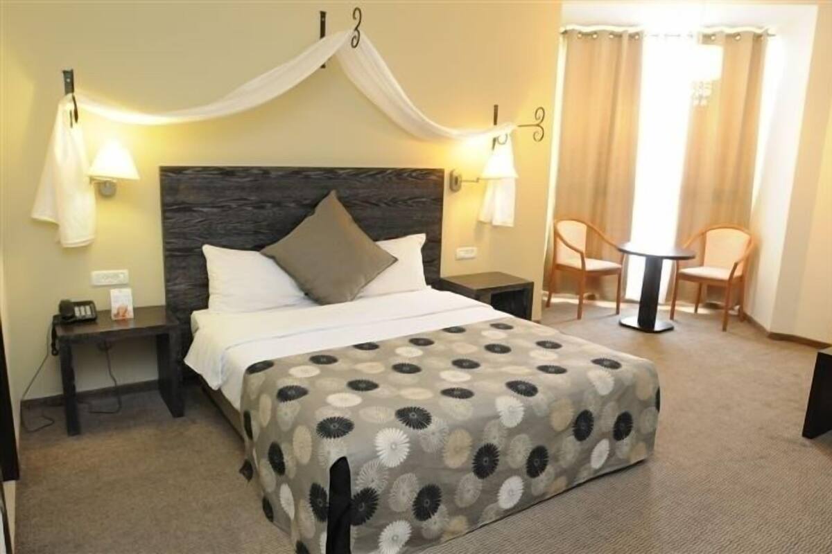 Une chambre d’hôtel comprenant un lit, une table de chevet, une commode, une chaise et une petite table.