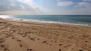 Une plage de sable où l’on peut voir des empreintes menant à l’eau, un ciel dégagé et un horizon lointain.