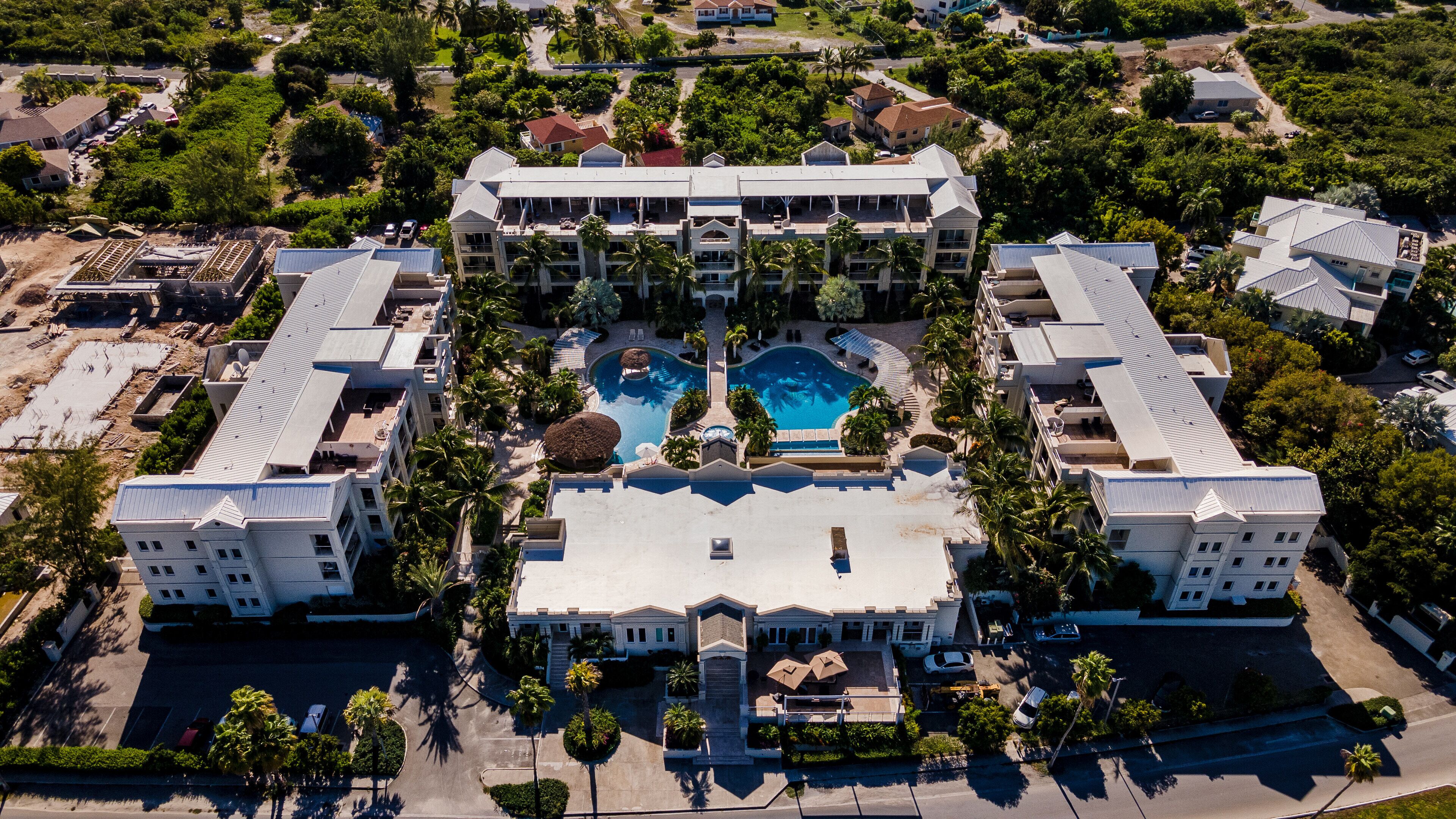An aerial view of a hotel with a central swimming pool, multiple buildings, and surrounding greenery.