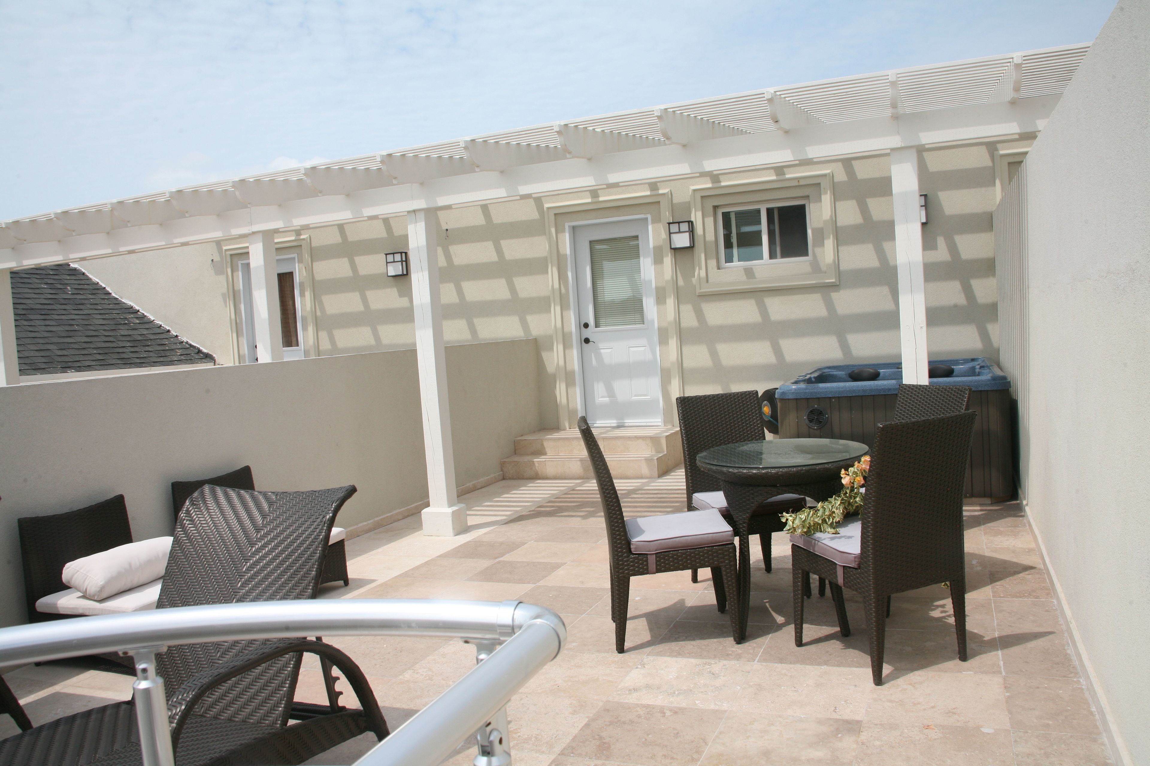 A patio with wicker furniture, a hot tub, and a door leading to a covered area.