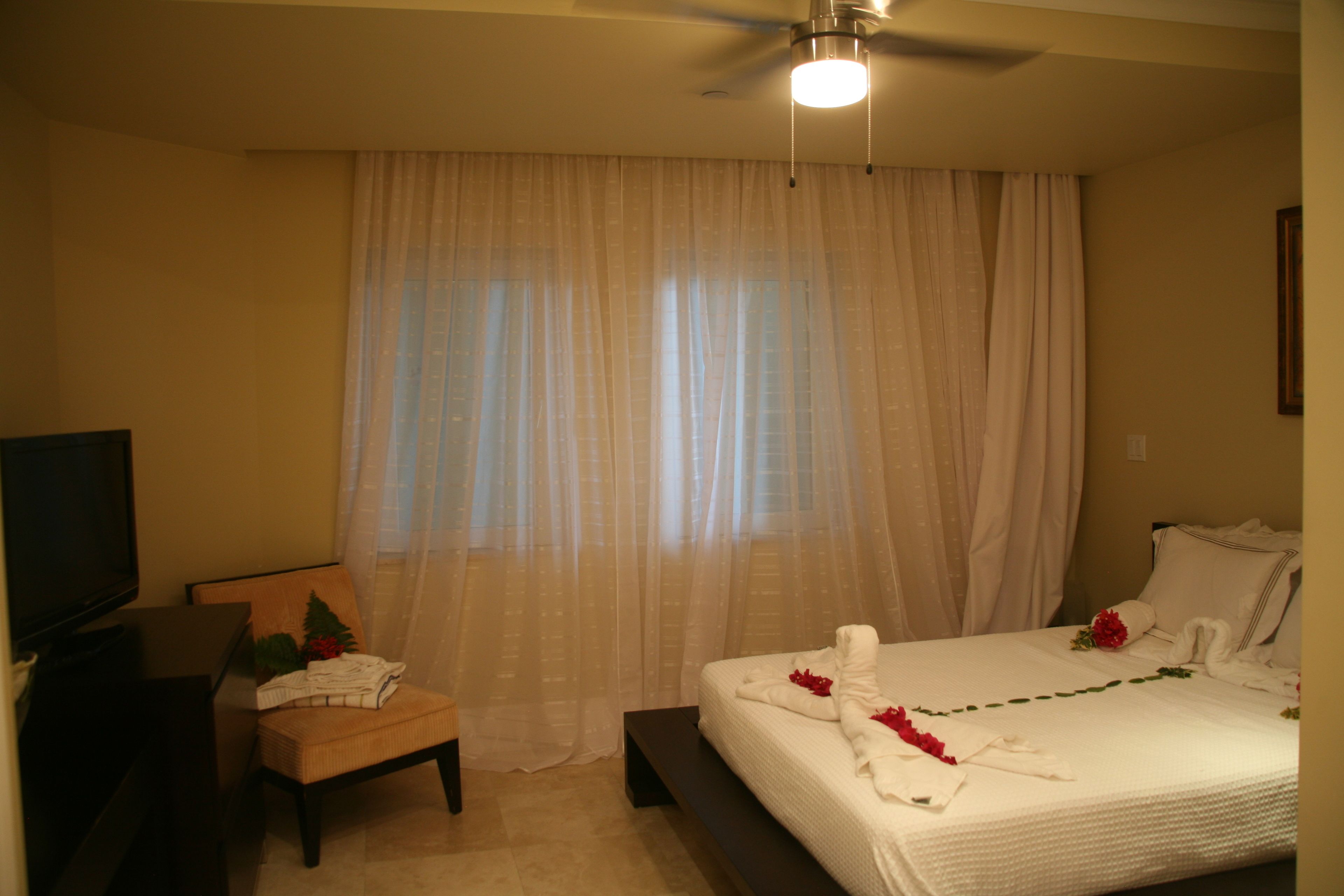 Habitación de hotel con cama, una silla, un televisor y un ventilador de techo.
