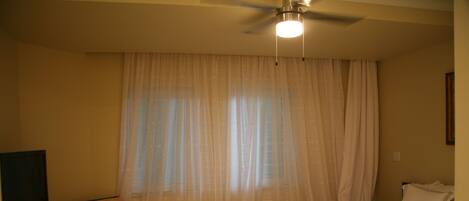 Habitación de hotel con cama, una silla, un televisor y un ventilador de techo.