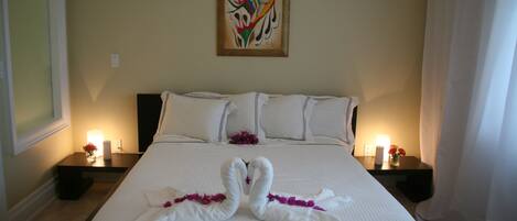 A neatly made bed with two swan-shaped towels, a painting on the wall, and bedside lamps.