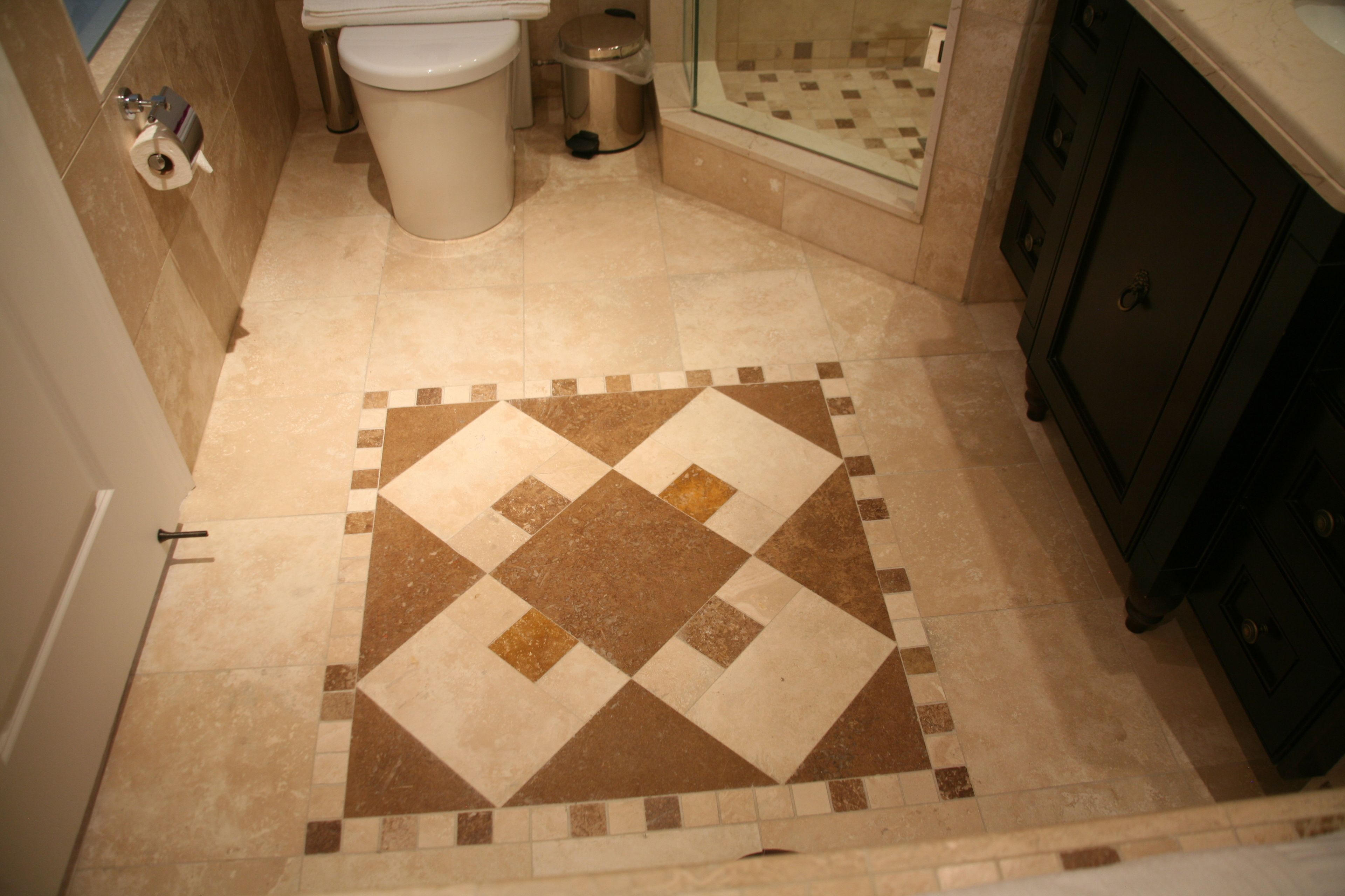 A bathroom with a patterned floor, a toilet, a trash can, and a shower area.